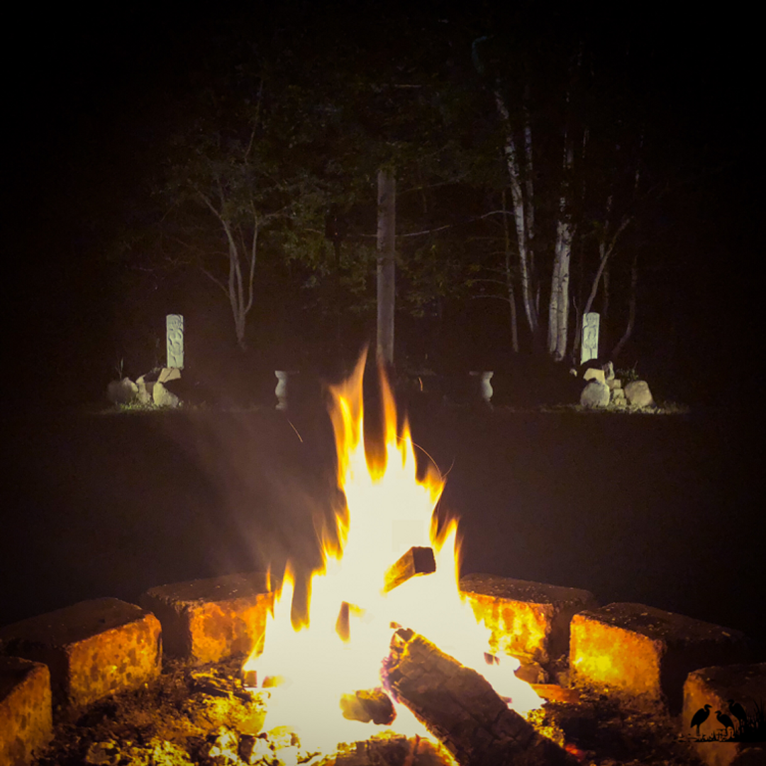 Fire in a pit at night, with sacred statues in the distance behind