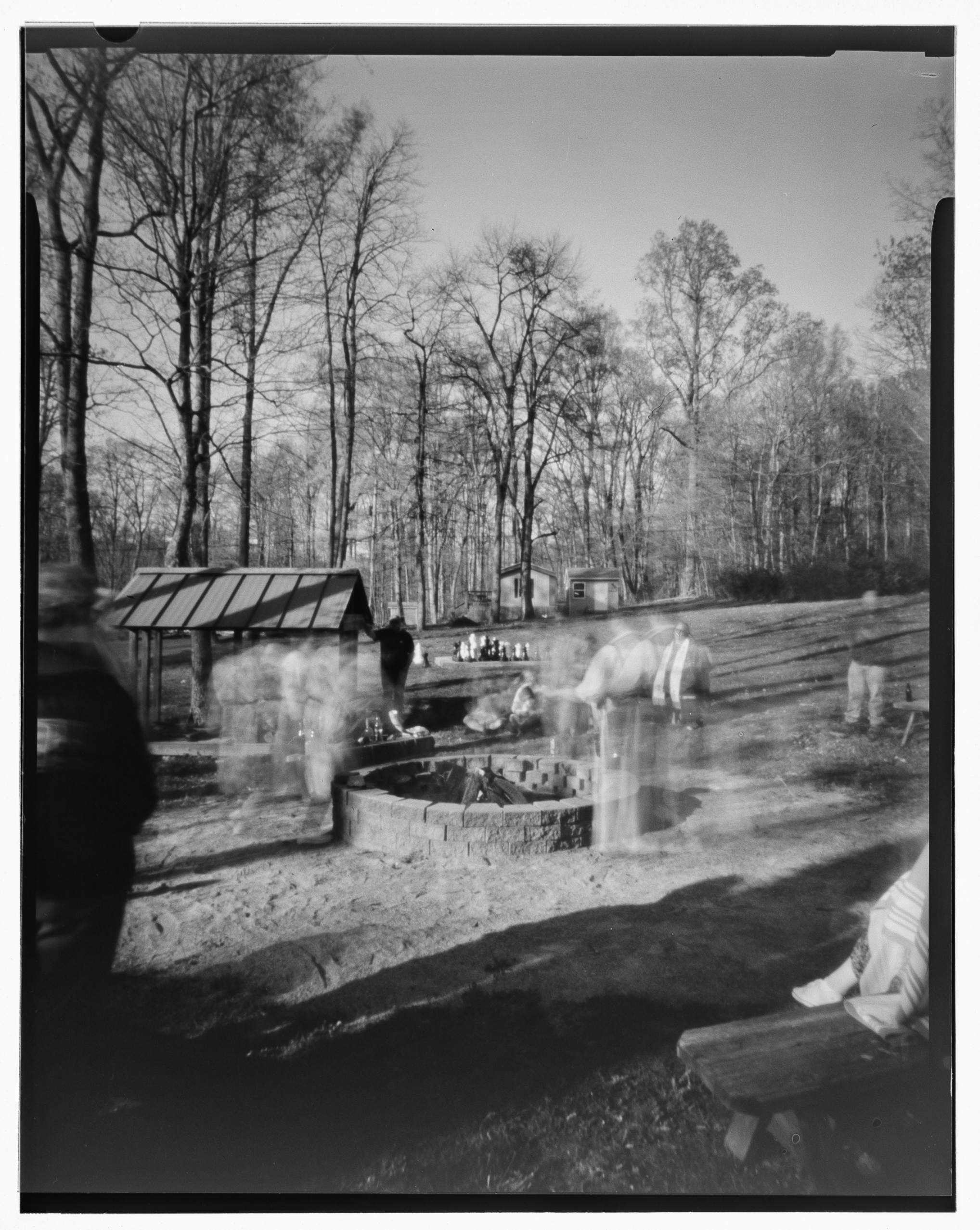 Black and white pinhole photo, with ghostly images of people making offerings around a central fire