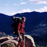 MJD wearing a hiking backpack on rocks, valley and mountains in background