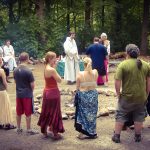 A group of people stand around a fire, with MJD at the center being ordained by Rev. Kirk Thomas