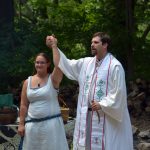 Rev. Dangler holding up Rev. Avende's hand in an outdoor ritual space