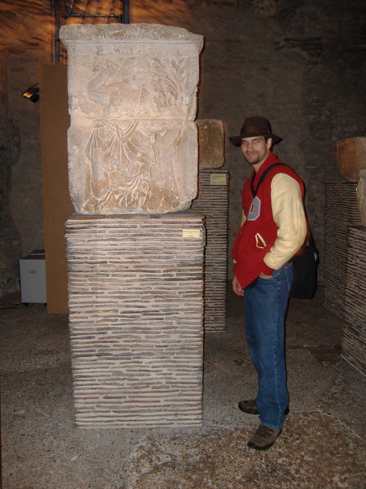 Rev. Dangler stands next to the Esus face of the Pillar of the Boatmen in a museum