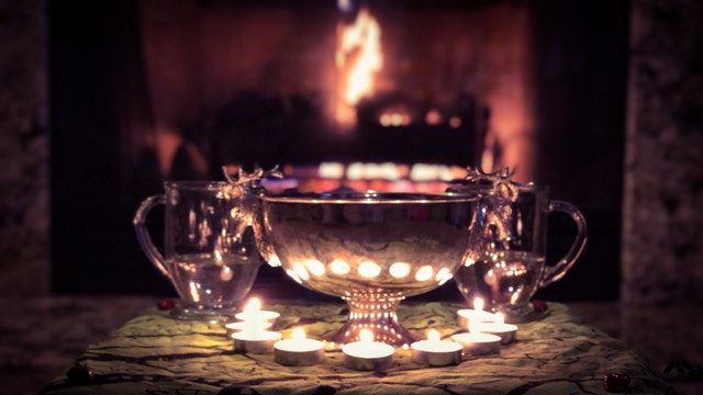 Candles surround a silver bowl, in front of a fire