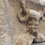 An antlered, bearded head with torcs hanging from the antlers, in profile