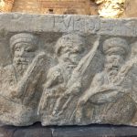 EVRISES is above three older men with hexagonal shields