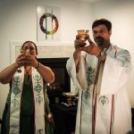 Rev. Avende and Rev. Dangler hold up cups of water, wearing ritual garb