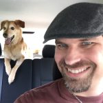 MJD in the front seat, and a happy-looking dog with paws on the back seat and tongue out behind
