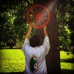 MJD holding up a wheel in front of a tree, a shaft of light hitting it