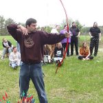 MJD fires an arrow from a bow while others watch behind him